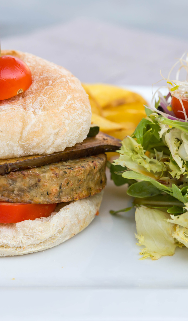 Большой гамбургер с салатом на столе 