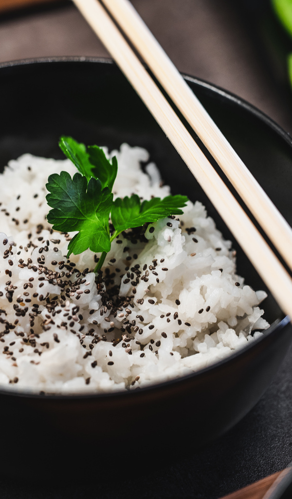 Вареный рис с семенами  в черной миске с палочками