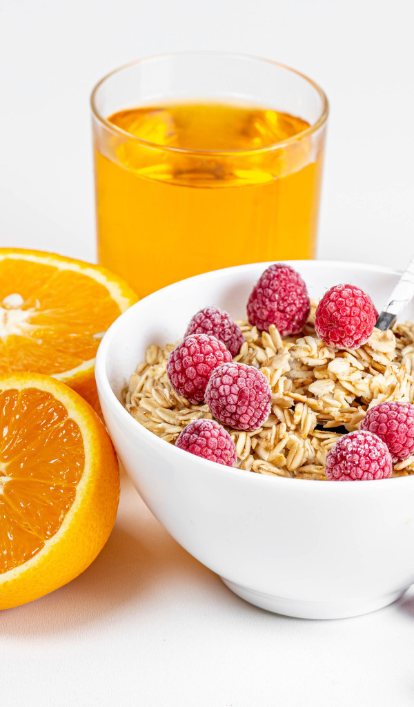 Миска мюсли с ягодами малины и апельсинами на столе с соком