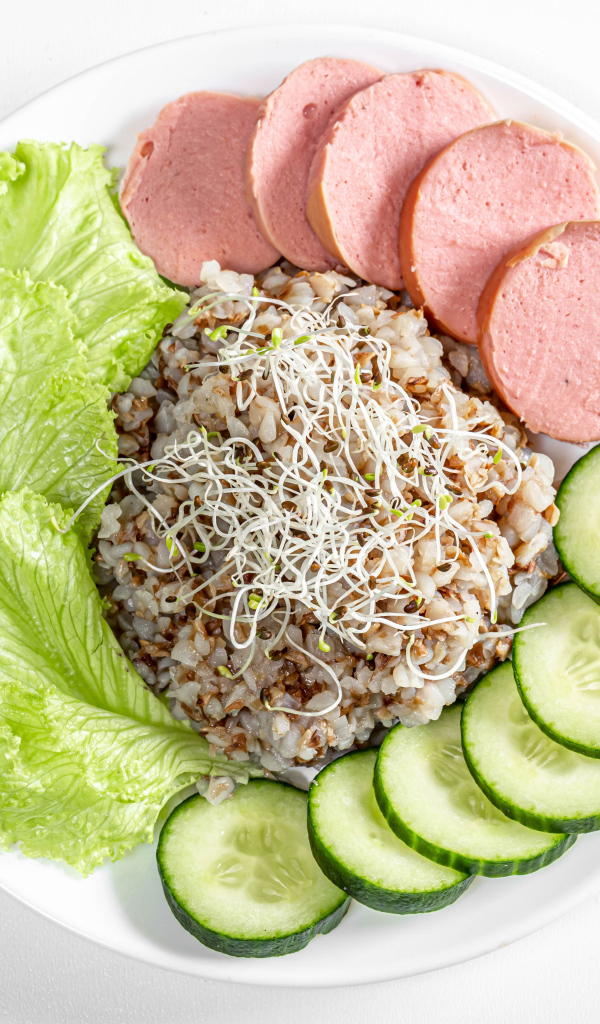 Buckwheat on a plate with cucumber, sausage and lettuce on a white background