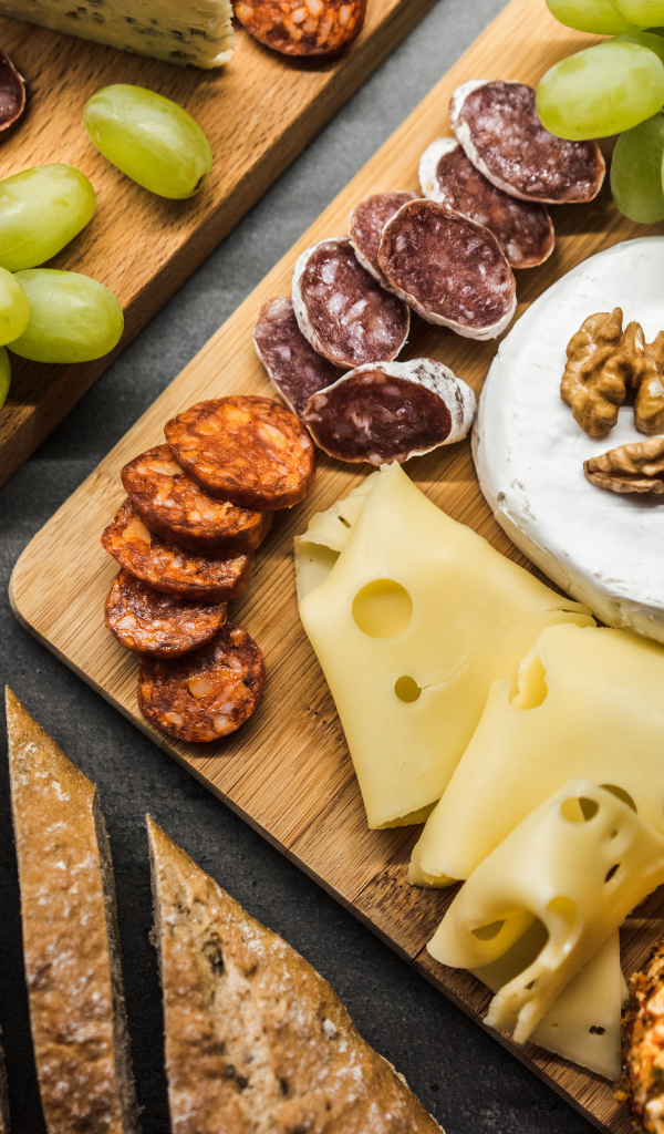 Сыр, колбаса, виноград и батон  на столе 