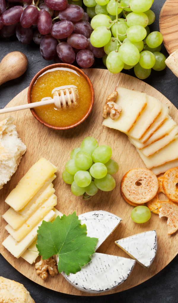 Сыр на столе с виноградом, оливками и белым вином