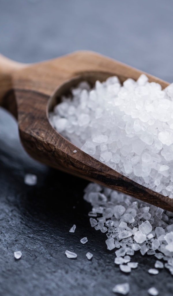Крупная белая соль в лопатке на столе 