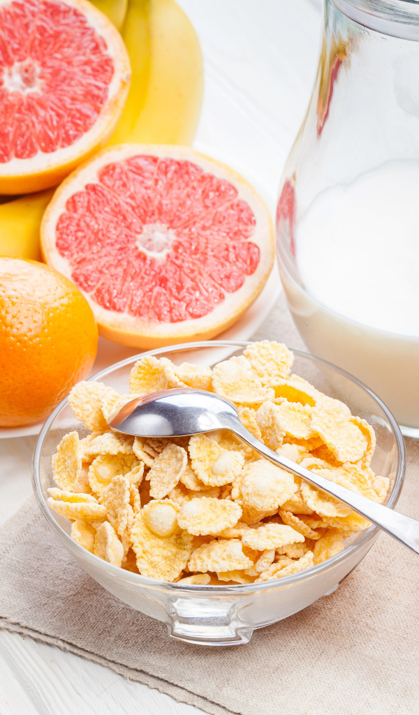 Кукурузные хлопья на столе с молоком, соком и свежими фруктами на завтрак