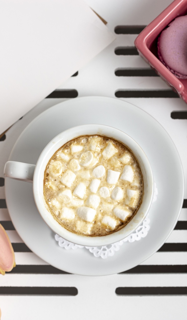 Чашка какао с маршмеллоу на столе с букетом тюльпанов, десертом макарун и очками