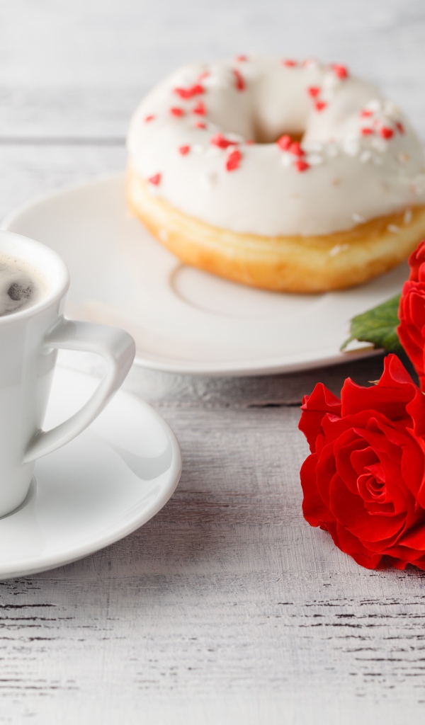 Чашка кофе, пончик и три красных розы на столе