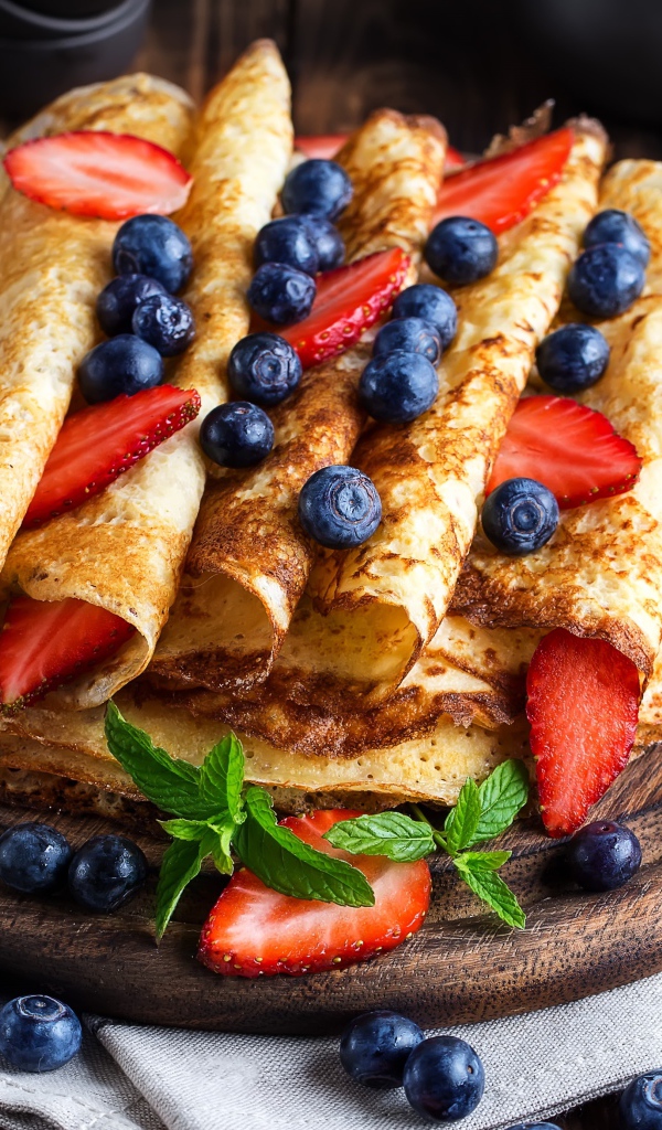 Вкусные тонкие блинчики на деревянной доске с ягодами черники и клубники 