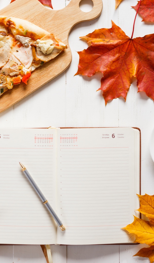 Ежедневник на столе с желтыми листьями, кофе и пиццей 