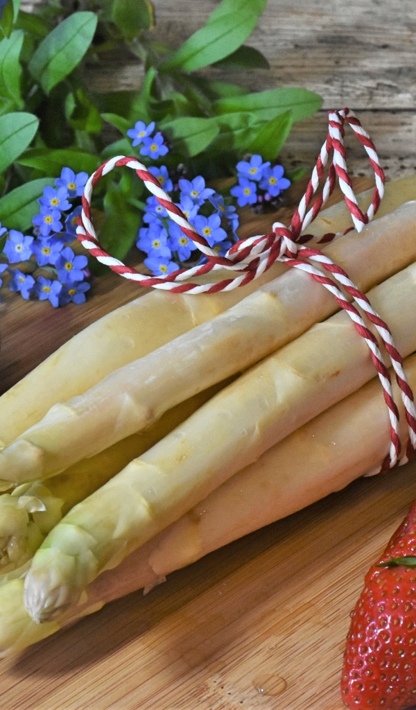 Свежая спаржа на столе с клубникой и цветами незабудками