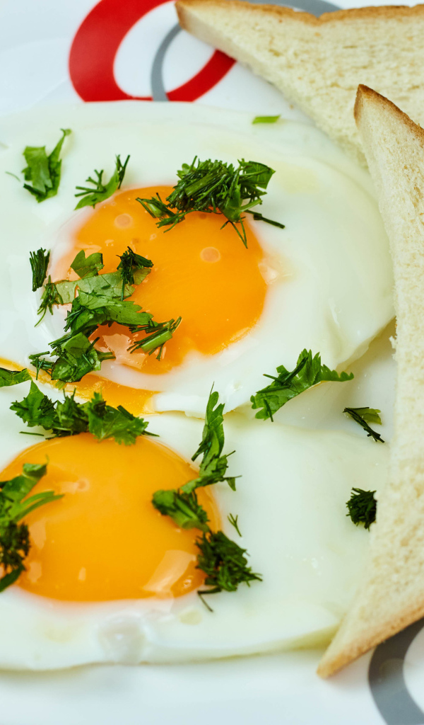Яичница глазунья с зеленью на тарелке с хлебом 