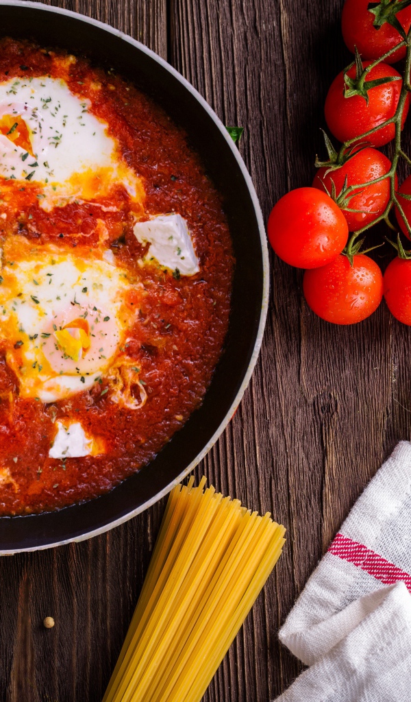 Греческое блюдо с томатами и яйцами на столе с спагетти и помидорами