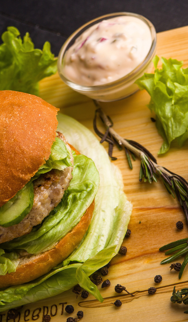 Гамбургер на столе с листьями салата, специями, помидорами и соусом