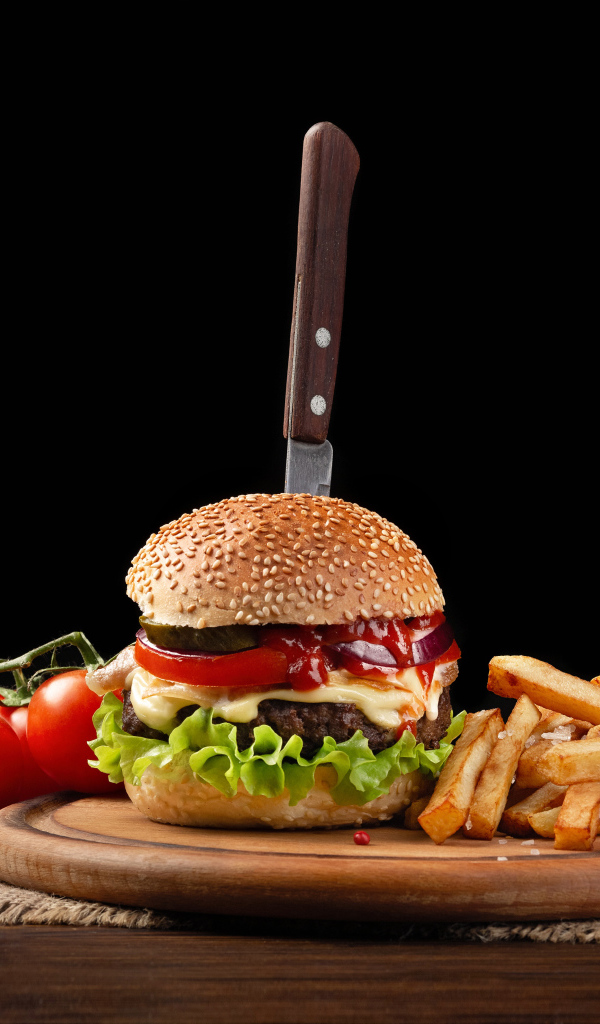 Гамбургер с ножом на столе с помидорами и картофелем фри 