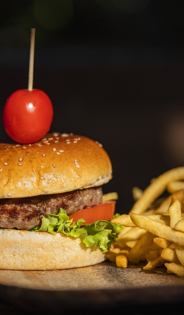 Гамбургер с помидором на доске с картофелем фри 