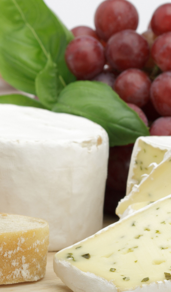 Твердый сыр на столе с батоном и виноградом