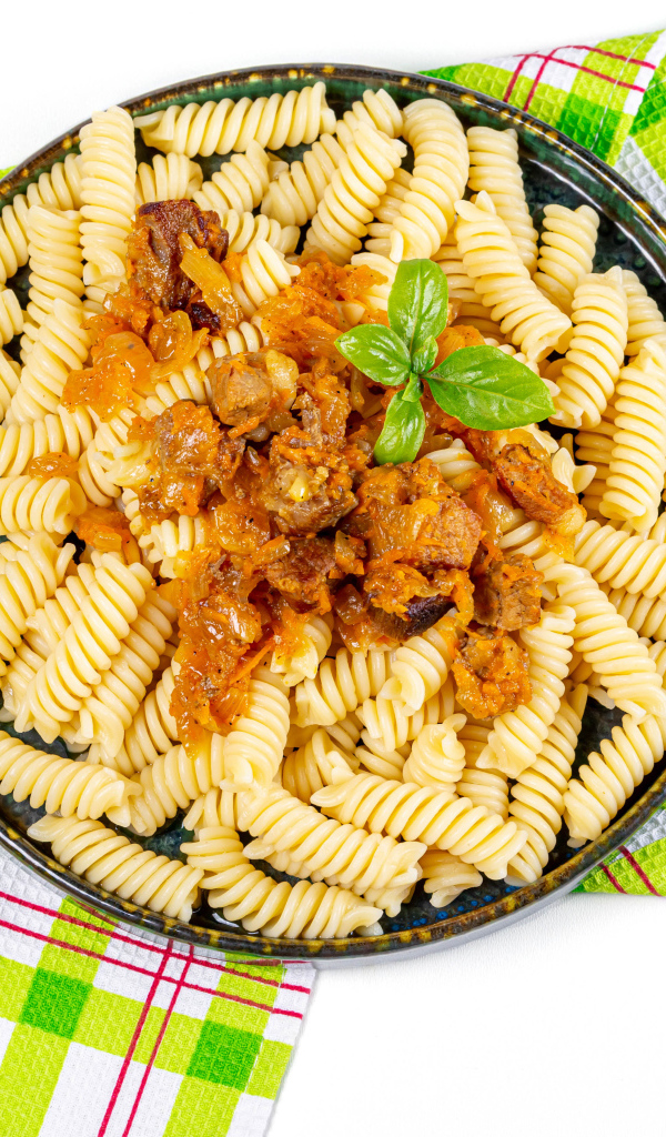 Большая тарелка макарон с мясом на столе со столовыми приборами