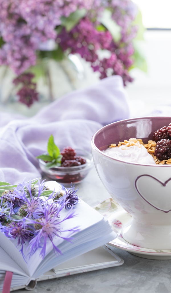 Мюсли с ягодами в чашке на столе с блокнотом и букетом сирени 