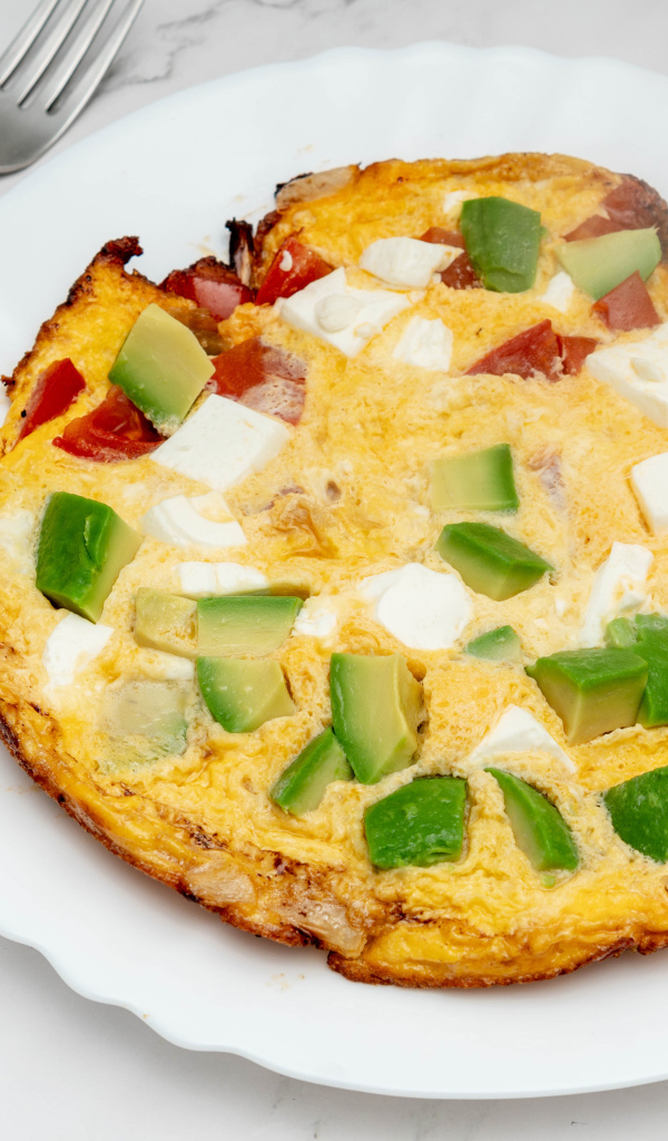 Омлет с авокадо и кусочками помидора на белой тарелке 