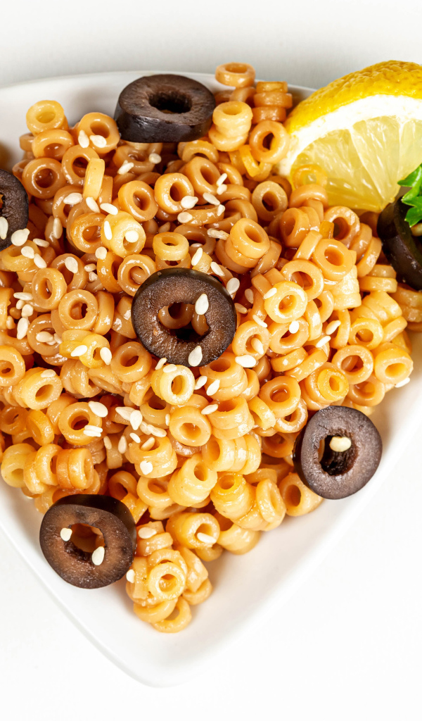 Макароны на тарелке с оливками и лимоном