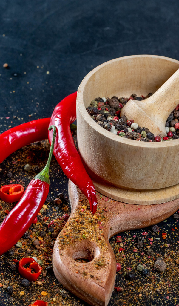 Перец горошком в ступке на столе с острым перцем