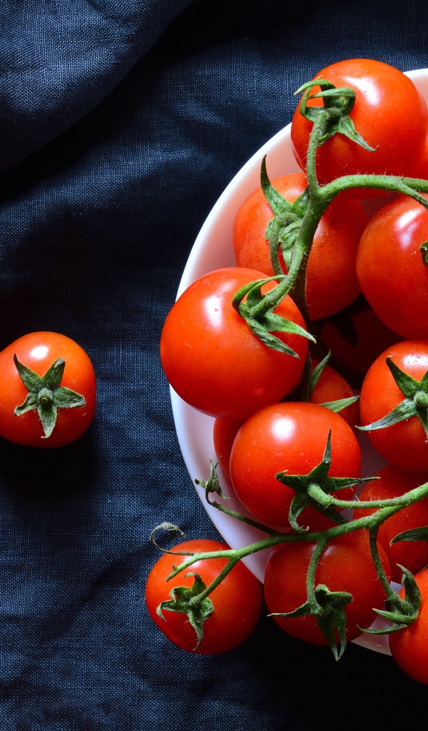 Красные помидоры в белой миске на черном фоне