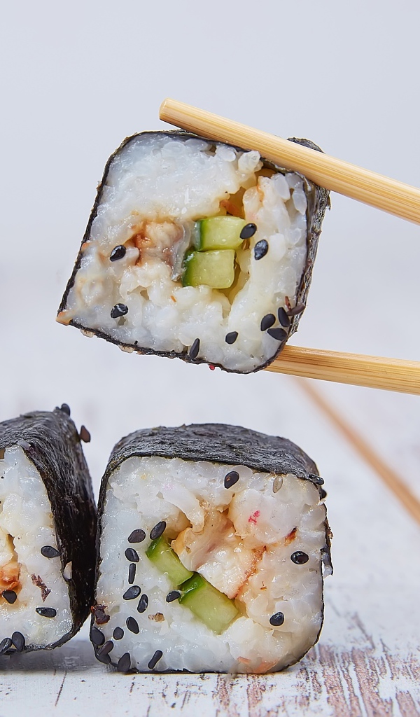 Роллы с рыбой и огурцом на столе с палочками
