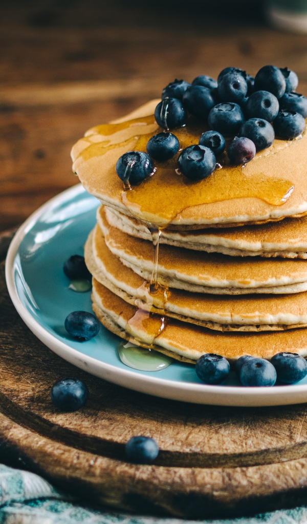 Румяные оладья на тарелке  с медом и ягодами черники 