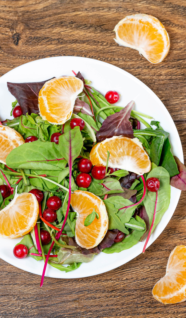 Салат из зелени и мандарина на белой тарелке на столе с вилкой