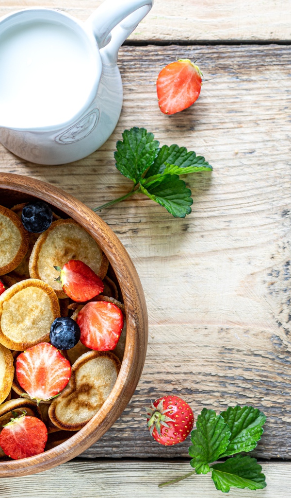 Маленькие оладьи в миске с клубникой и черникой на столе с молоком 