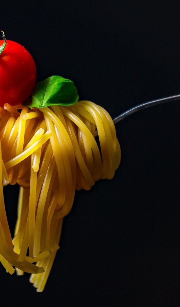 Спагетти с помидором на вилке на черном фоне