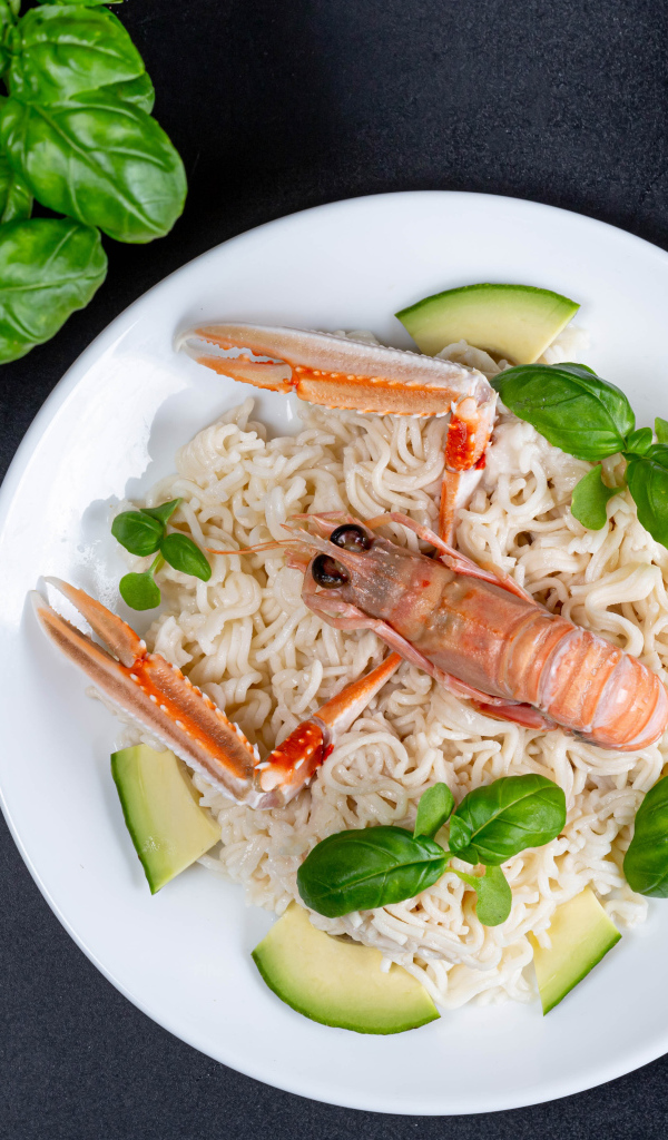 Вермишель с омаром на тарелке с авокадо и листьями базилика 