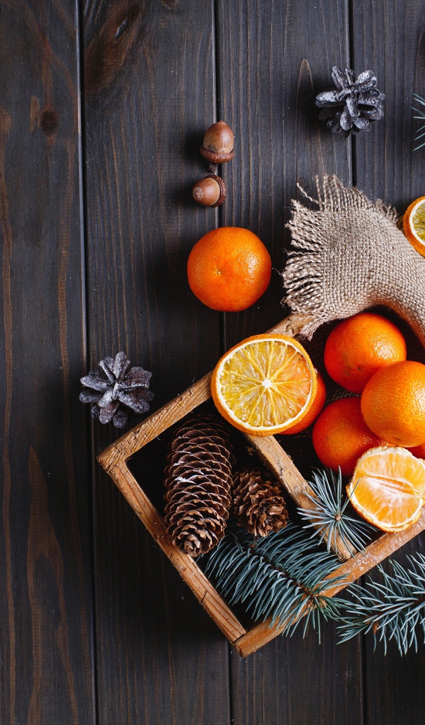 Ящик с мандаринами и шишками на столе с еловыми ветками