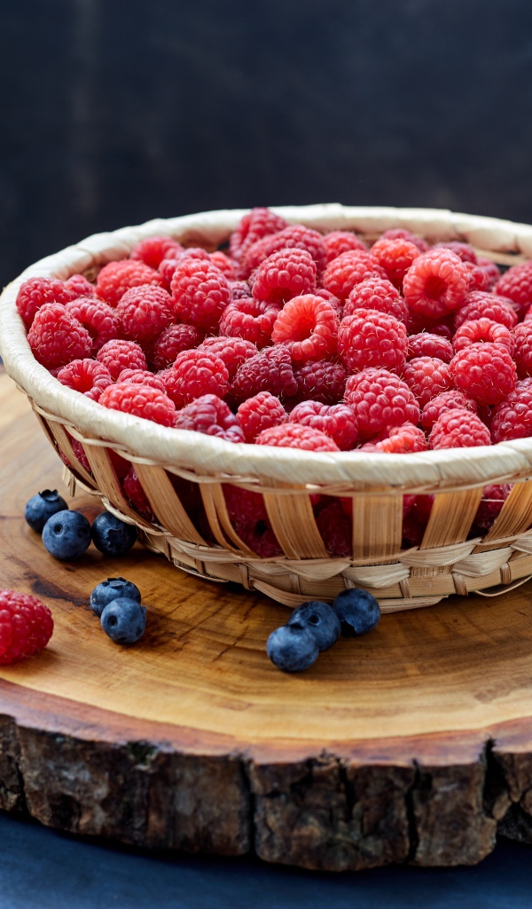Корзинка с малиной на столе с ягодами черники