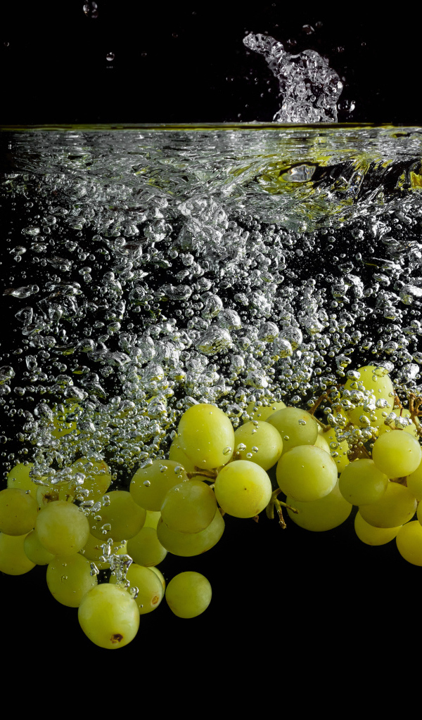 Ягоды белого винограда в воде на черном фоне