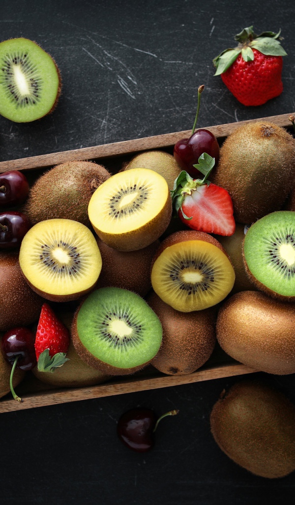 Ящик с киви, клубникой и черешней на столе 