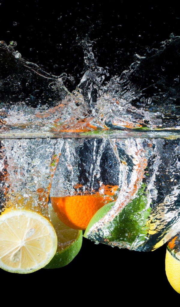 Цитрусовые фрукты падают в воду на черном фоне