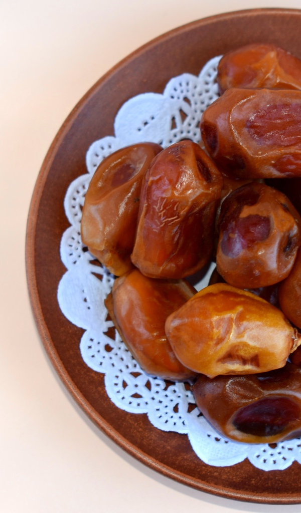 Сушеные финики в деревянной миске на белом фоне