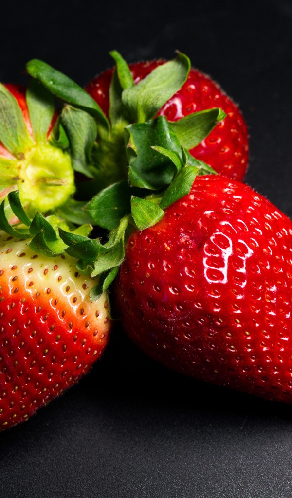 Четыре спелых красных ягоды клубники на черном столе 