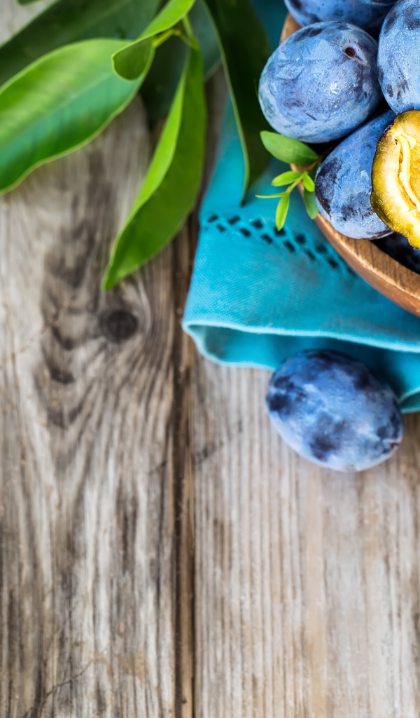 Свежие синие сливы с зелеными листьями на столе 