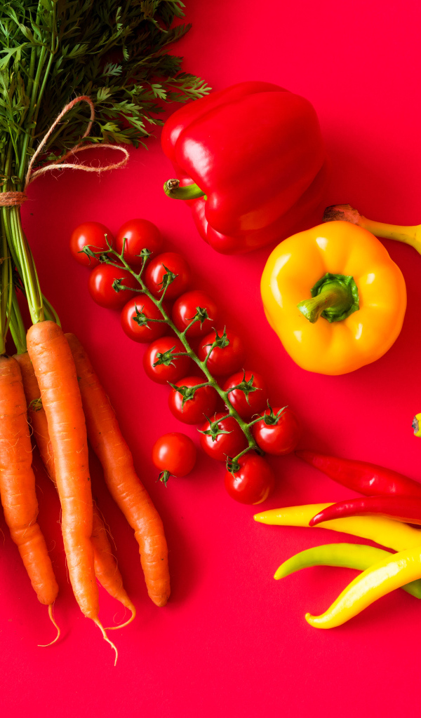 Свежие морковь, помидоры, перец и бананы на красном фоне