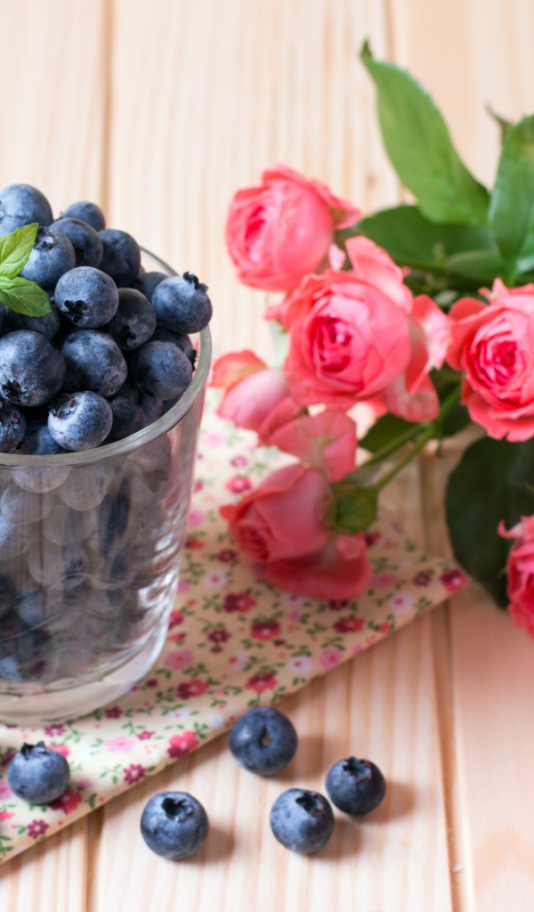 Glass of blueberries on the table with a bouquet of pink roses