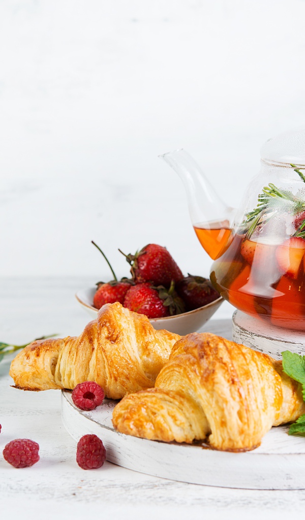 Чайник с лимоном и клубникой на столе с круассанами 