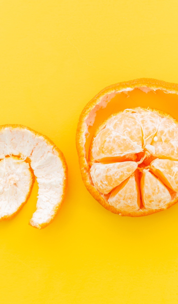 Очищенный мандарин с кожурой на желтом фоне 