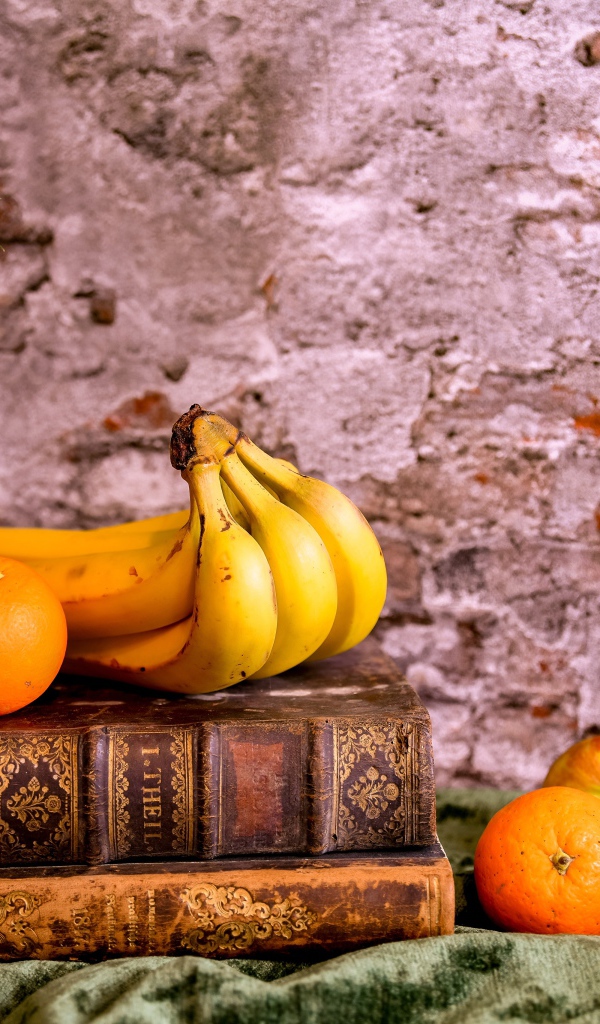 Ананас, бананы, апельсин и яблоки лежат на столе с книгами