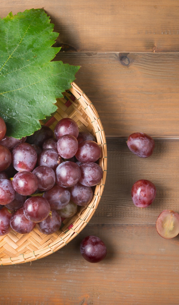 Розовый виноград с зелеными листьями на деревянном столе 