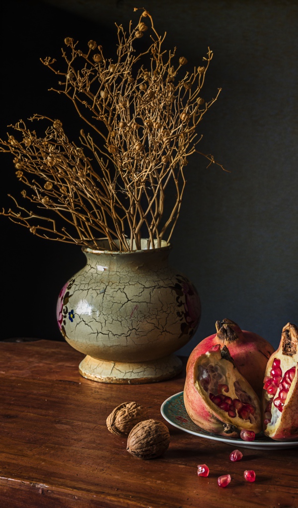 Красный гранат на столе с грецкими орехами и сухой веткой в вазе