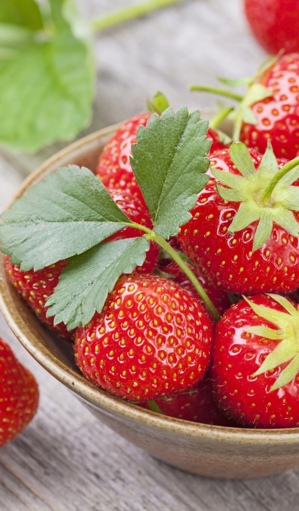 Красная спелая сладкая клубника в тарелке с зелеными листьями