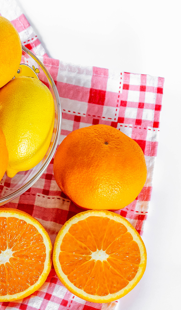 Спелые апельсины и лимоны в стеклянной миске на столе