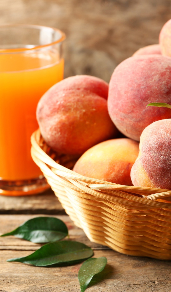 Спелые персики в корзине на столе с соком