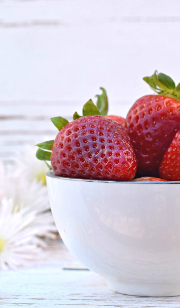 Спелая клубника в белой миске на столе с ромашками